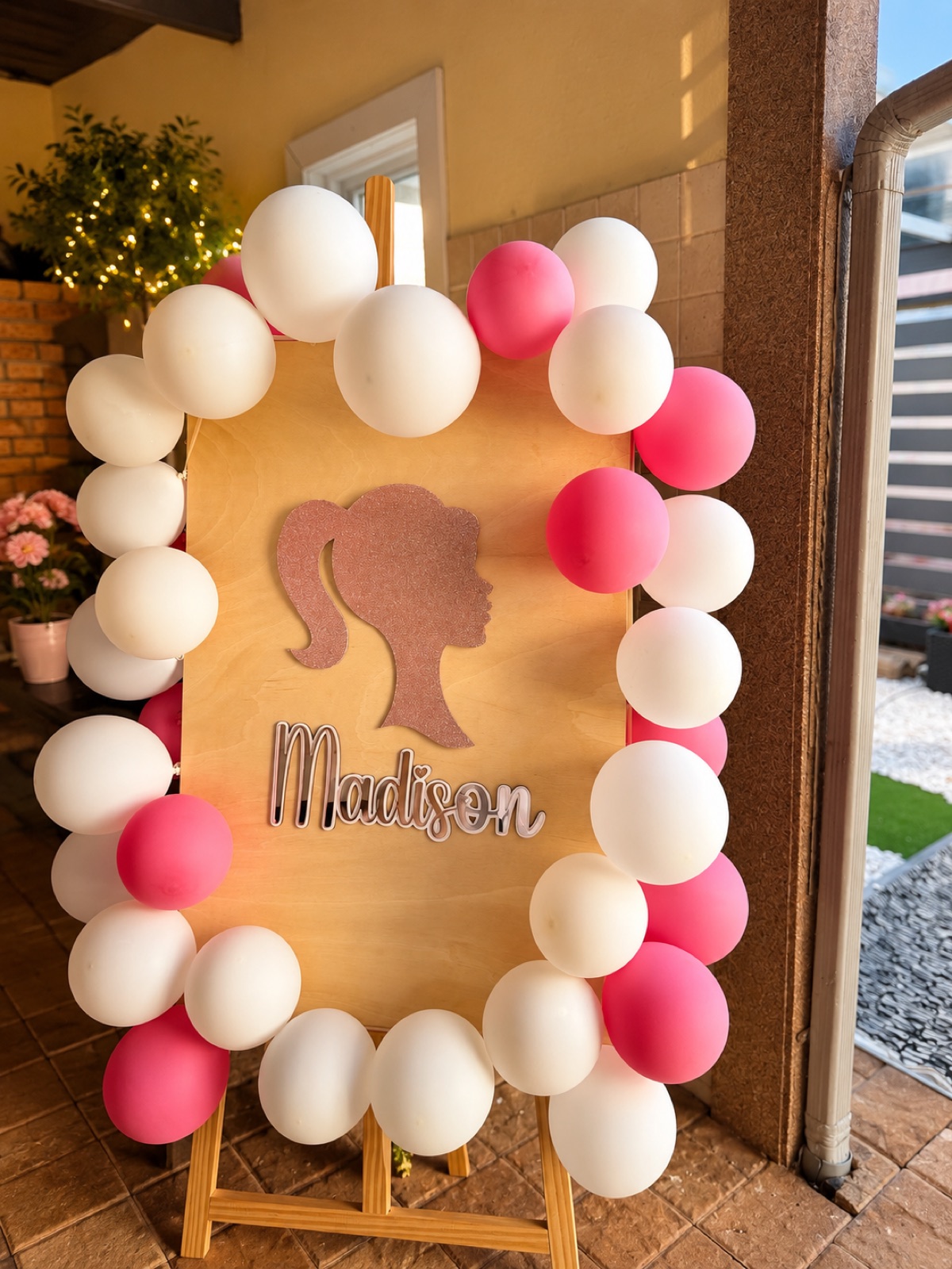 Painel de boas-vindas em madeira com nome em acrílico rosa-dourado e arco de balões, de uma festa personalizada da Organize Sua Vida